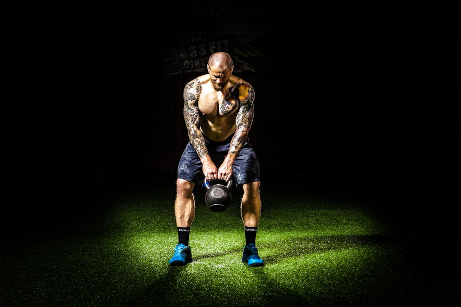 Muscular man with tattoos lifting a kettlebell indoors under a spotlight. Intense fitness and strength training