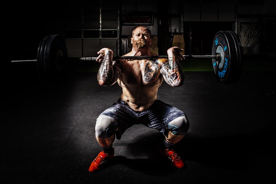 A tattooed man performing a heavy barbell squat in a gym for strength training.